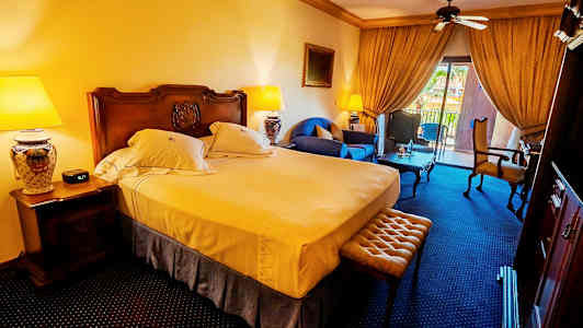 Ett hotellrum med en dubbelsäng, sittmöbler och en balkong med utsikt. (AI-genererad text)