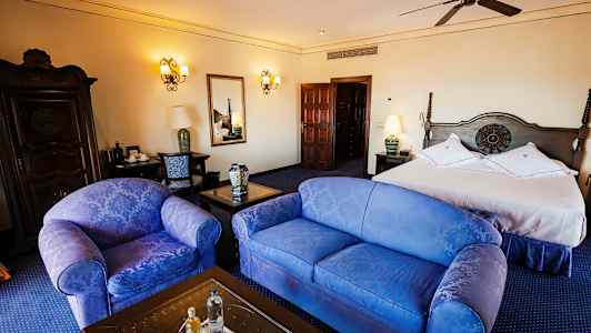 Ett hotellrum med en dubbelsäng, två stolar, ett bord och en byrå, elegant inrett. (AI-genererad text)