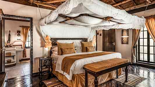 Ett elegant sovrum med himmelssäng, bruna dekorativa element och trägolv. (AI-genererad text)