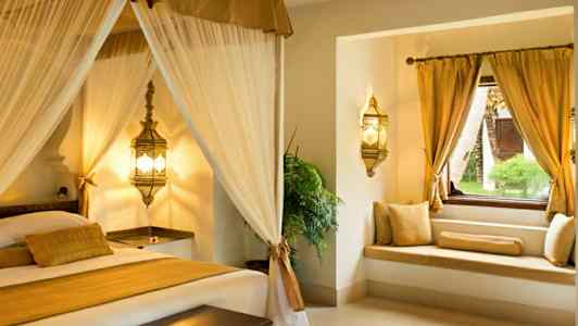 En elegant sovrumsinteriör med himmelssäng och fönstersits med guldkuddar. (AI-genererad text)