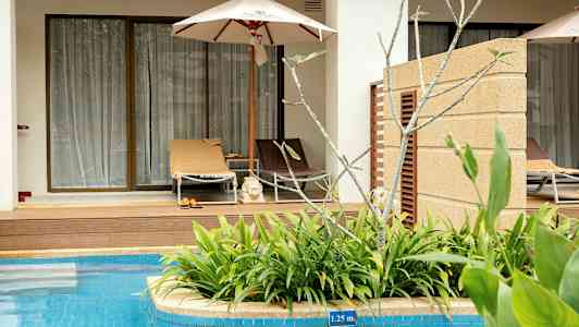 En solstol med parasoll framför en terrass vid en pool. (AI-genererad text)