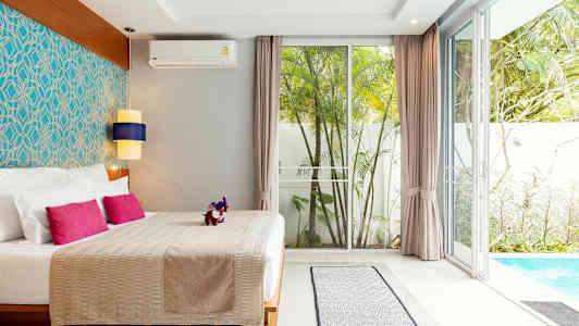 Ett sovrum med dubbelsäng, färgglada kuddar, stilfull inredning och utsikt mot en pool och trädgård. (AI-genererad text)