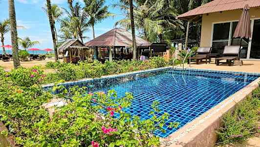 En pool omgiven av blommor och växter med palmer och en strand i bakgrunden. (AI-genererad text)