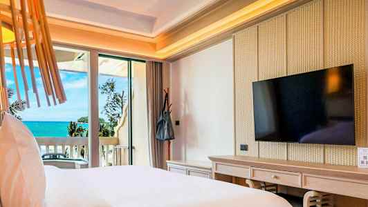 Hotellrum med bäddad säng, väggmonterad TV och balkong med utsikt över havet. (AI-genererad text)