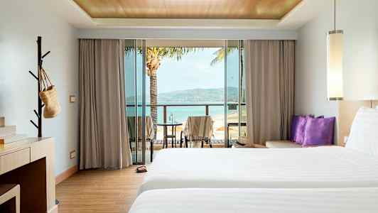 Hotellrum med två sängar, skrivbord och balkong med utsikt över stranden. (AI-genererad text)