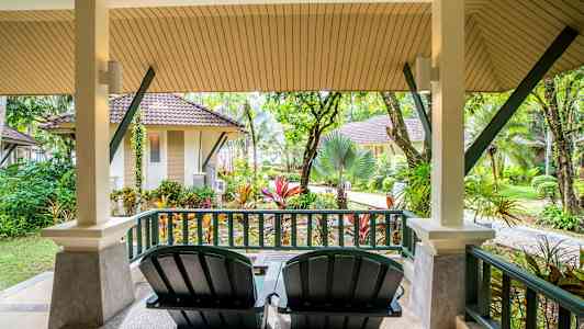 Veranda med två stolar och utsikt över trädgård och små hus. (AI-genererad text)