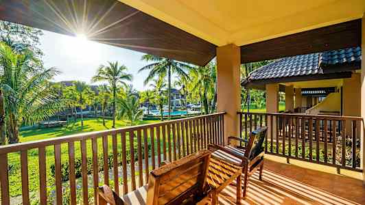 Utsikt från en balkong med sittmöbler mot en trädgård med palmer. (AI-genererad text)