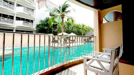 Utsikt från en balkong med vita stolar mot en swimmingpool och omgivande byggnader. (AI-genererad text)