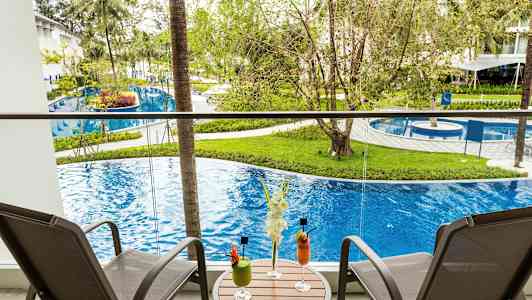 Balkong med två stolar och ett bord med drinkar, utsikt över pool och grönska. (AI-genererad text)