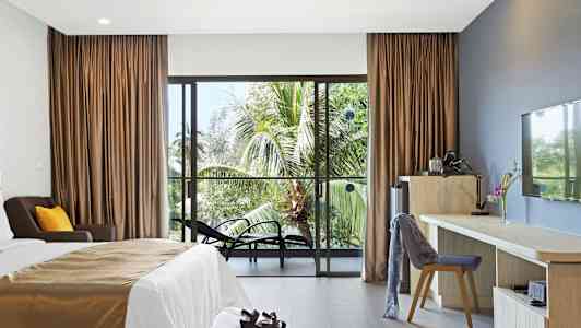 Hotellrum med en säng, skrivbord och stolar, samt utsikt mot palmer genom en glasdörr. (AI-genererad text)