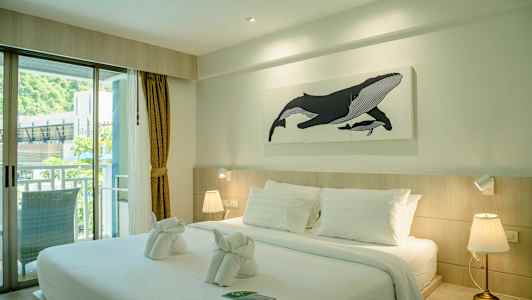 Ett hotellrum med en stor säng, vita sängkläder, och en målning av en val på väggen. (AI-genererad text)