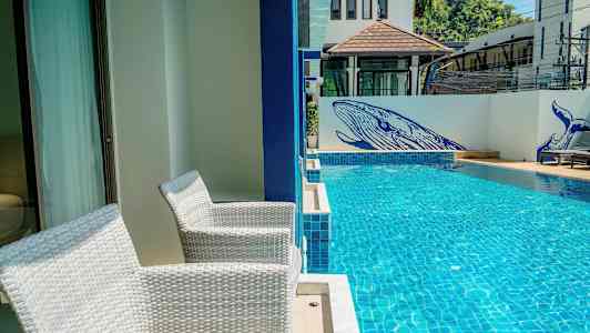 Två vita stolar står vid en terrass bredvid en simbassäng. På väggen vid bassängen finns blå målningar av valar. (AI-genererad text)