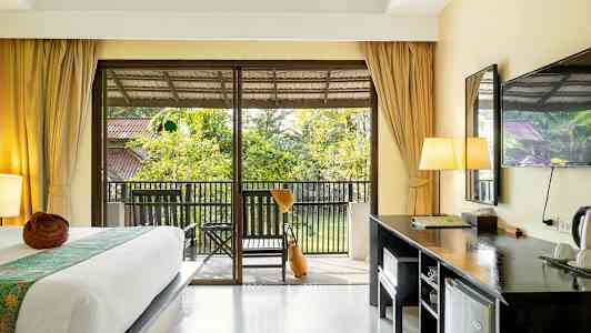 Ett hotellrum med en säng, skrivbord och en balkong med utsikt över trädgård. (AI-genererad text)