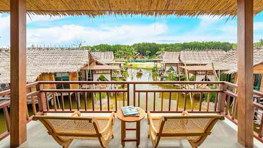 Två stolar och ett litet bord på en veranda med utsikt över hyddor vid vattnet. (AI-genererad text)