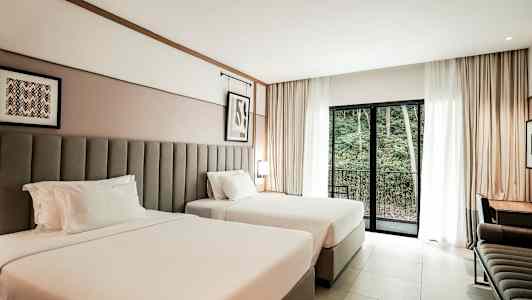 Ett hotellrum med två breda sängar, ett skrivbord och en balkongdörr med utsikt över skogsområde. (AI-genererad text)