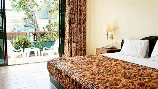 Bild på ett hotellrum med dubbelsäng och en balkong med utemöbler. (AI-genererad text)