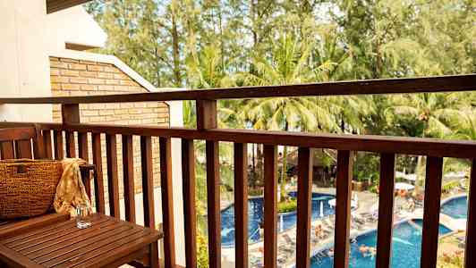 Utsikt från en balkong mot en pool och omgivande träd. (AI-genererad text)