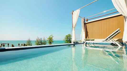 En lyxig pool med en solstol bredvid och en havsutsikt i bakgrunden. (AI-genererad text)