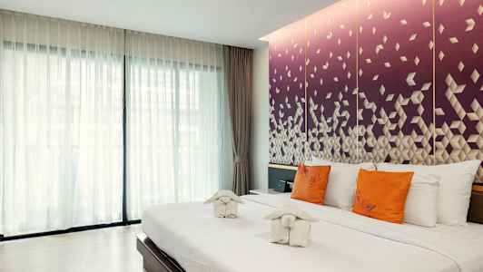 Ett hotellrum med en stor säng, vita sängkläder, orange kuddar och dekorativa handdukar. Bakgrunden visar en lila vägg med geometriskt mönster. (AI-genererad text)