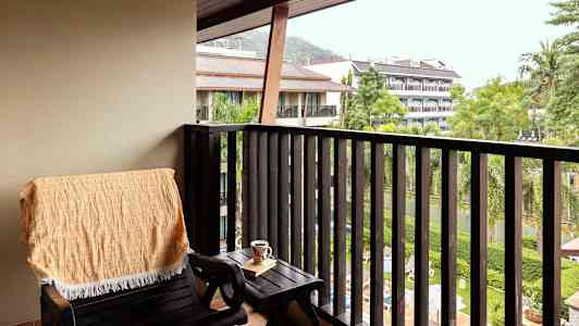 En balkong med en stol, ett bord och utsikt över grönska och byggnader. (AI-genererad text)