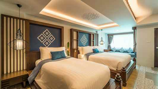 Ett hotellrum med två breda sängar, dekorerade med vita lakan och blå kuddar, samt ett stort fönster med gardiner. (AI-genererad text)