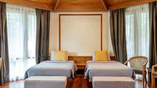 Hotelrum med två enkelsängar, träinredning och stora fönster med gardiner. (AI-genererad text)