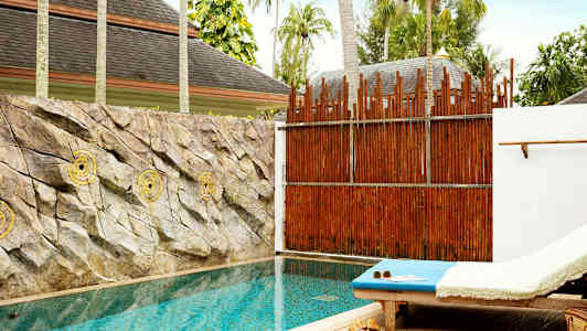 En privat pool med solstol bredvid och stenar pryder väggen bakom poolen. (AI-genererad text)