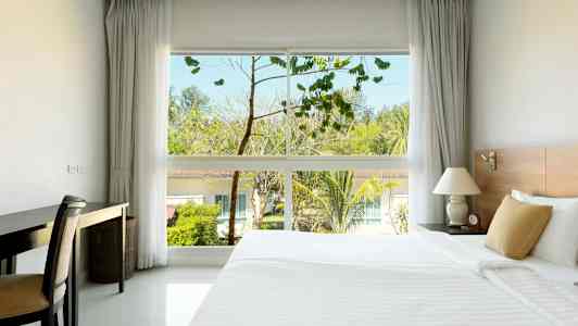 Ett hotellrum med en stor säng, ett skrivbord och ett fönster som visar träd och byggnader utomhus. (AI-genererad text)