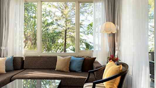 Vardagsrum med soffa och kuddar framför fönster med utsikt mot grönska. (AI-genererad text)