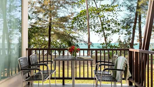 Utsikt från en veranda med bord och stolar, med havet och träd i bakgrunden. (AI-genererad text)