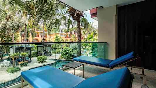 Utsikt från en balkong med två blåa solstolar som vetter mot en färgglad trädgård med palmer och pool. (AI-genererad text)