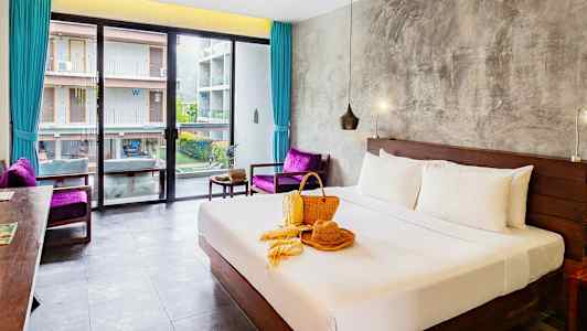 Hotellrum med en bäddad dubbelsäng, fönster mot en byggnad och dekoration på sängen. (AI-genererad text)