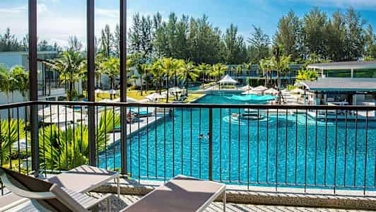 En pool omgiven av byggnader och palmer, sett från en veranda med solstolar. (AI-genererad text)