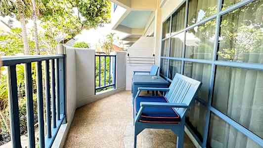 Bild på en balkong med två blå stolar, bord och utsikt mot träd och grönska. (AI-genererad text)