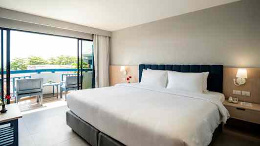 Hotellrum med dubbelsäng, sängbord och utsikt mot balkong. (AI-genererad text)