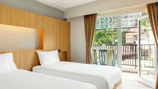 Två enkelsängar i ett hotellrum med stora glasdörrar mot en balkong. (AI-genererad text)