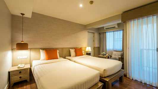 Två enkelsängar med orange kuddar i ett rum med trädetaljer och gardiner som släpper in ljus. (AI-genererad text)