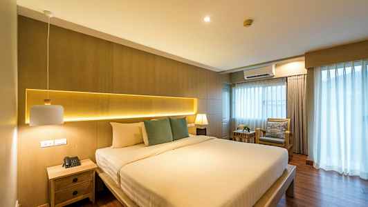 Sovrum med en stor säng, sidobord och fönster med gardiner. (AI-genererad text)