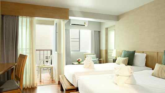 Ett hotellrum med två enkelsängar, vita sängkläder och gröna prydnadskuddar. Det finns en uteplats med stolar och ett bord. (AI-genererad text)