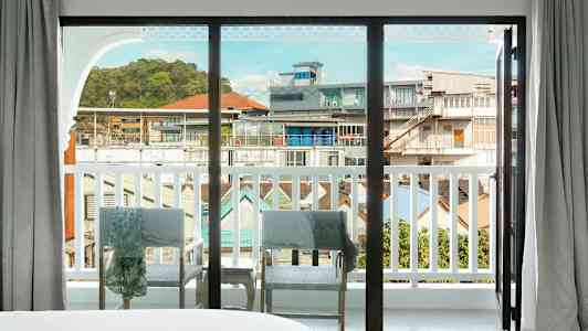 Vy genom ett stort glasfönster som öppnar mot en balkong med utsikt över stadsmiljön. (AI-genererad text)