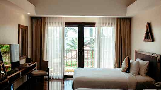 Ett hotellrum med två sängar, ett skrivbord med stol, och stora fönster med utsikt mot en balkong och träd utomhus. (AI-genererad text)