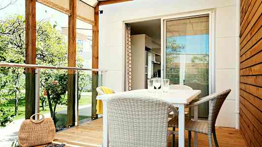 En veranda med tak, bord och stolar samt utsikt mot en trädgård. (AI-genererad text)