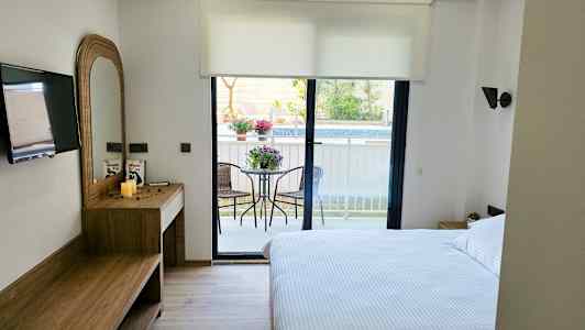 Ett hotellrum med en dubbelsäng, skrivbord, TV och en balkong med trädgårdsmöbler. (AI-genererad text)