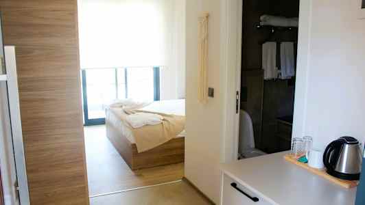 Interiör av ett hotellrum med säng, badrum och tekokare på en bänk. (AI-genererad text)