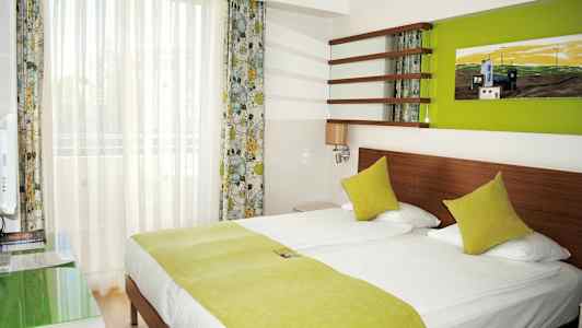 Ett hotellrum med en dubbelsäng och gröna sängkläder. (AI-genererad text)