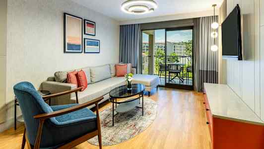 Ett vardagsrum med soffa, fåtölj, soffbord och utsikt mot en balkong. (AI-genererad text)