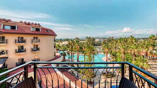 Utsikt från en balkong över en hotellbyggnad, en pool och palmträd. (AI-genererad text)