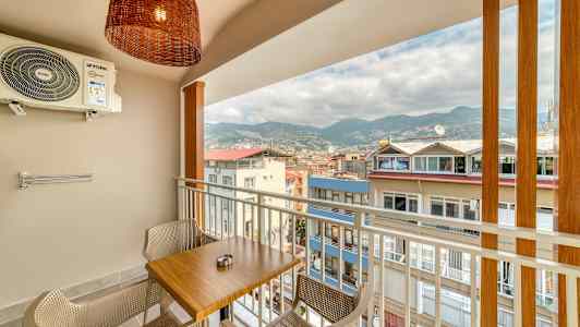 Balkong med ett bord och två stolar, utsikt över byggnader och berg. (AI-genererad text)