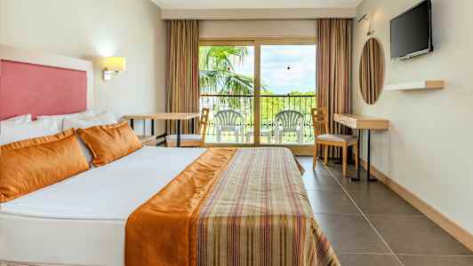 Interiör av ett hotellrum med en stor säng, en balkong med sittmöbler och en TV på väggen. (AI-genererad text)