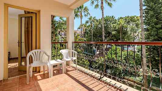 Balkong med en dörr, två vita plaststolar och utsikt över träd och vegetation. (AI-genererad text)